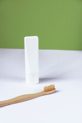 White tube of toothpaste and toothbrush on white table against green wall background. Personal hygiene and self-care concept