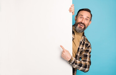 Photo portrait of man smiling hiding behind empty white wall showing copyspace promo isolated...
