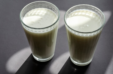 Two full glasses of kefir on a gray surface with shadows.