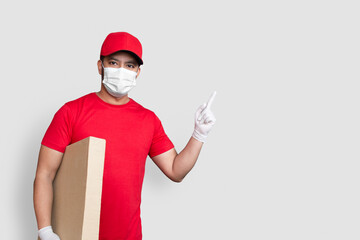 Delivery man employee in red cap blank t-shirt uniform face mask hold empty cardboard box isolated on white background