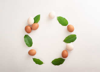 Easter decoration in the form of a round wreath of white and brown eggs and green leaves on a white background. place for text. copy space. flat lay