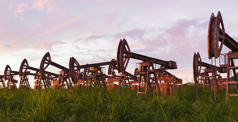 landscape with rusted and abandoned oil pumps and grass growing around it with sunset. climate...