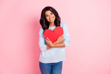 Photo of positive romantic lady cuddle red paper heart card toothy smile wear blue sweater isolated pink background