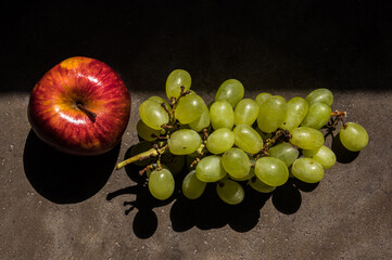 A red apple and green grapes structure background in natural light in an artistic way.
