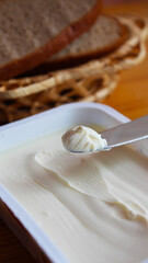 Cream cheese in a plastic rectangular box is taken on a knife. Well-fed breakfast. Selective focus and blurred background.