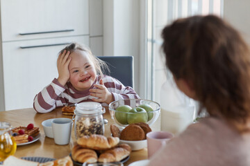 Portrait of cute girl with down syndrome enjoying breakfast with family at home and smiling happily...
