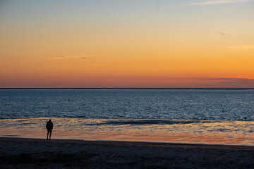 View of silhouettes of people walking in the setting sun shining on the Sea and reflected on the beach, clouds with sun-shining edges. Landscape. High quality photo showing concept of freedom and
