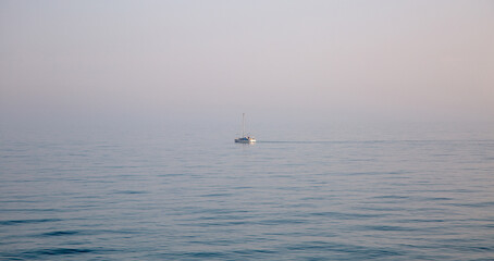 Obraz premium lonely boat in the blue ocean in the morning with gog in the background.
