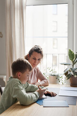 Vertical side view portrait of caring single mother helping son doing homework in cozy home...