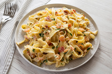 Homemade Garlic Shrimp Bacon Alfredo on a plate on a white wooden background, side view.
