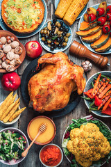 Christmas or Thanksgiving whole roasted chicken, rice, pumpkin, corn, honey, nuts, vegetable salads over wooden background. Autumn harvest, organic vegetables. Autumn family dinner. Food concept