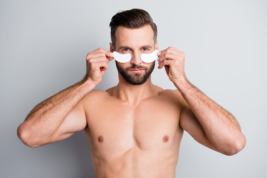 Close-up portrait of attractive fit athletic guy applying patch under eye correction anti age isolated over light grey pastel color background - Powered by Adobe