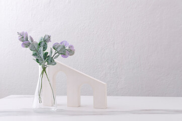 Decorative arch stand, glass vase and eucalyptus leaves on the white table against bright wall