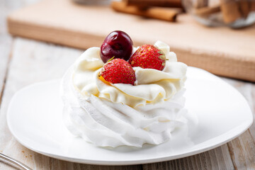 Pavlov dessert with whipped whites and berries on the wooden background