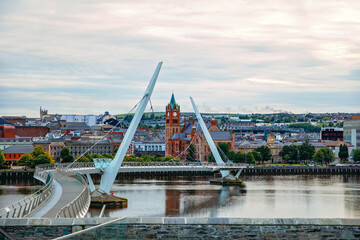 Derry, Ireland. Illuminated Peace bridge in Derry Londonderry, City of Culture, in Northern Ireland with city center at the background. Night cloudy sky with reflection in the river at the dusk
