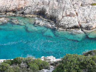 Fototapeta premium Colorful turquoise seawater seen from a cliff with trees. Amazing colors in the sea.  Narrow sea gulf between grey beige limestone rocks. 