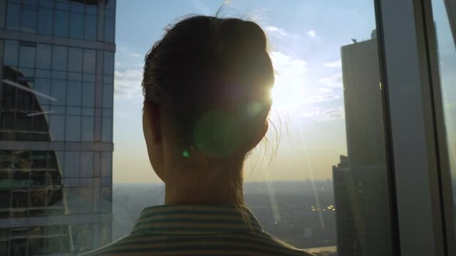 Success, opportunity, sightseeing, discover and future concept. Back view of pensive woman silhouette looking at cityscape through window of skyscraper. Summer time, sun lens flare, daylight
