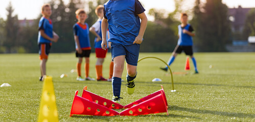 Children football player with training hurdles. Soccer agility training equipment. Kids playing sports on grass field. Happy boys practice sports. Kids football speed training