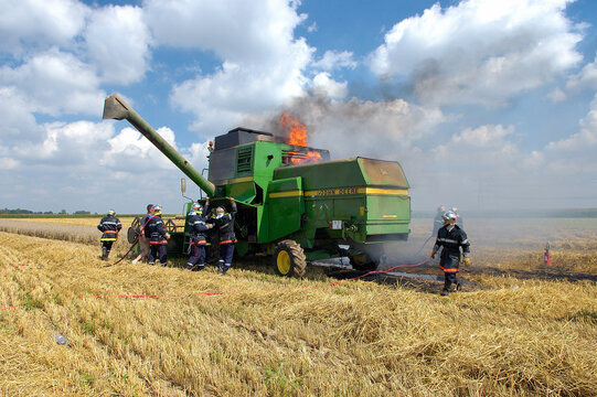 Incendie d'une moissonneuse dans un champ pendant une moisson de bl&eacute;. Intervention pompiers pour &eacute;teindre l'incendie
