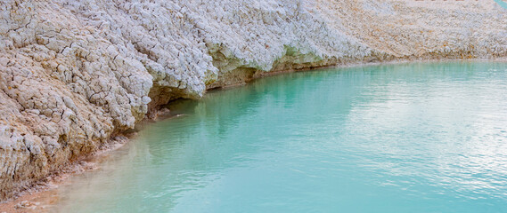 Shore with white clay close-up, turquoise azure water in pond, shallow lake with clear blue water.