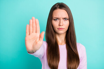 Photo portrait of frowning woman showing palm telling you to stop isolated on vivid teal colored...