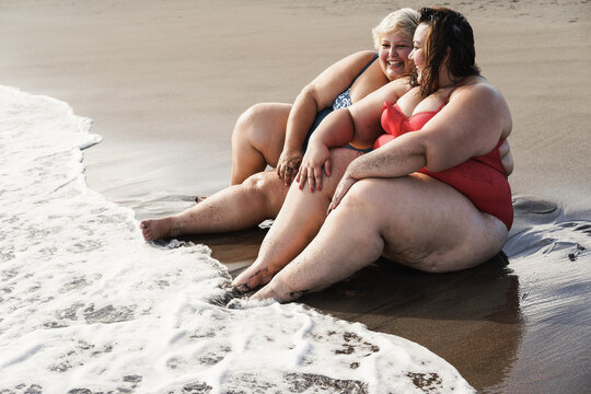 Plus size women sitting on the beach having fun during summer vacation - Focus on right face