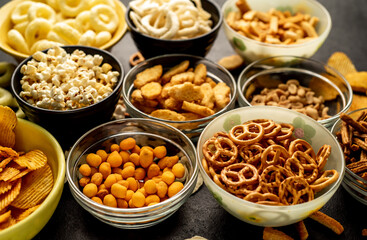 Assorted chips, popcorn, onion rings, croutons, cheese balls, biscuits in bowls. unhealthy food for figure, heart, skin, teeth. An assortment of fast carbohydrates. Junk food on a stone background