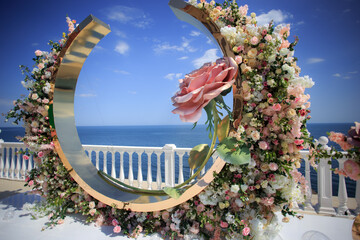 Luxurious wedding ceremony on the ocean coast. Floristic composition in the form of an arch of decorative and live roses.