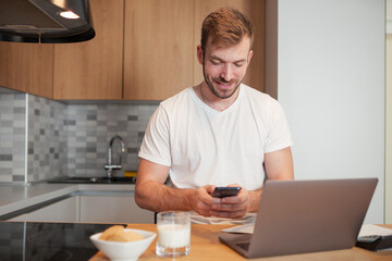 Fototapeta na wymiar Caucasian handsome man working on laptop at morning in kitchen