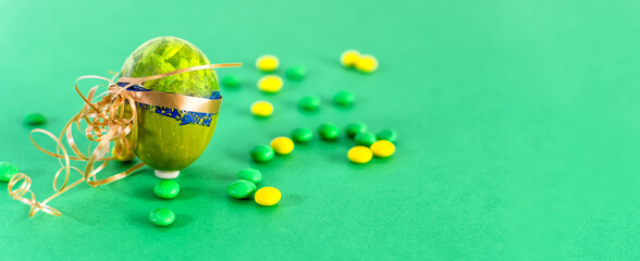Green Easter egg and candies on a light green background.