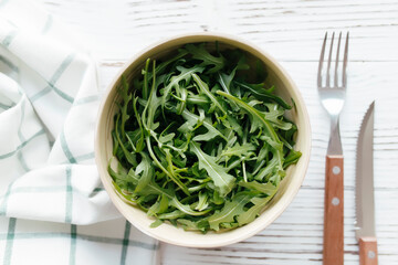 Green arugula salad leaves in bowl on wooden background. Healthy eating concept