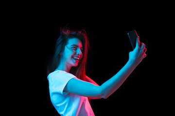 Young beautiful girl with smartphone isolated on dark background in neon light