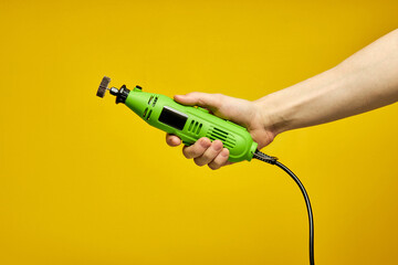 Green Die grinder in hands isolated on yellow background