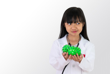 Asian child girl in a white doctor's uniform holds a green ball that looks like a virus or bacteria in her hand and a smiling face.