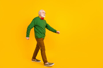 Full length photo of cute positive age gentleman wear sweater bowtie spectacles walking looking empty space isolated yellow color background