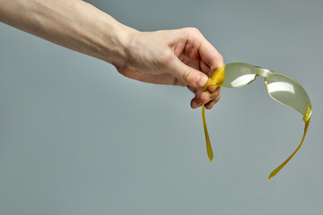 Yellow safety glasses in male hands isolated on gray background