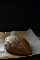 Edge of fresh dark loaf of bread on black background. Yeast product.