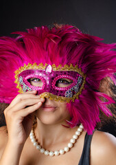 Beautiful young Brazilian woman with brown hair wearing a Venetian mask, dark background, selective focus.