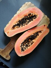 Papaya. Orange tropical fruit with black seeds inside on wooden cutting board and gray background.