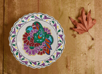Handmade buta ornament a ceramic plate  with autumn leaf on a wooden background. Azerbaijan, Baku. 07.03.2021