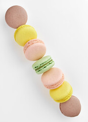 Vertical photo of macaroon. Colorful cakes macaron with pastel tones laid out in a strip from the corner of the frame to another corner on white background. Top view of almond cookies.