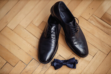 Leather classic brown shoes with a red insole on a wooden floor near the belt and bow tie. Set of gentleman and groom for the wedding.