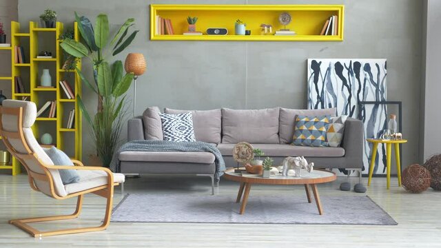 Grey corner sofa in the room with yellow niche, pillow, lamp, vase of plant, middle table, carpet, poster and rocking chair.