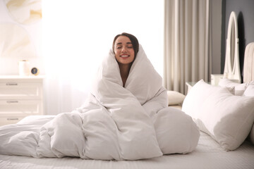 Beautiful young woman wrapped with soft blanket on bed at home - obrazy, fototapety, plakaty