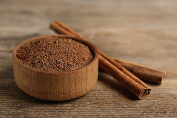 Aromatic cinnamon powder in bowl near sticks on wooden table, closeup