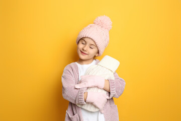 Ill girl with hot water bottle suffering from cold on yellow background