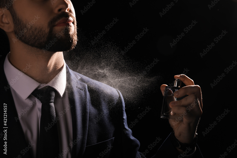 Poster man spraying luxury perfume on black background, closeup