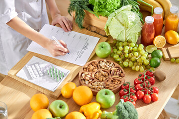 Cropped dietitian, nutritionist or doctor standing by desk writing about benefits of eating fresh...