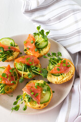 Delicious hearty appetizer, salmon toast on a white plate, round fried bun with red fish, cucumber, hollandaise sauce and pea sprouts