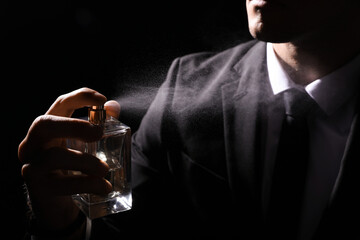 Man spraying luxury perfume on black background, closeup